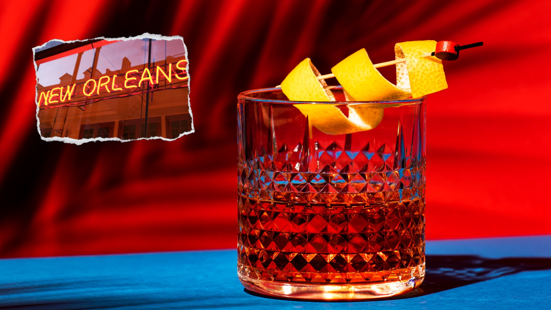 Cocktail Sazerac decorato con scorza di limone e sulla sinistra una scritta che fa riferimento alla città di New Orleans